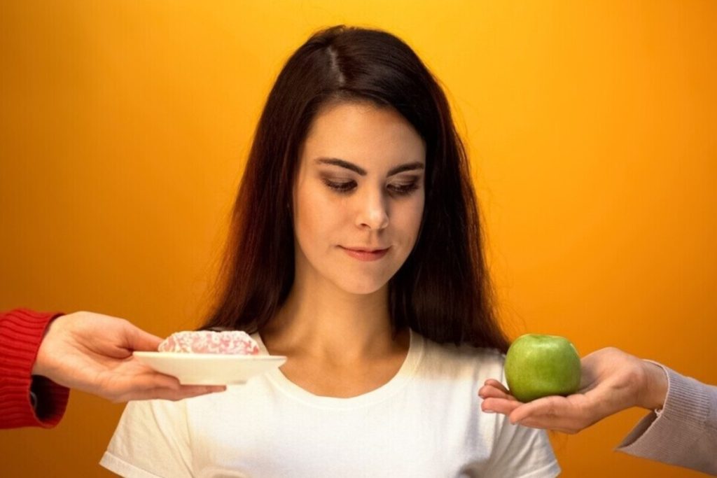 Žena gleda u krofnu i jabuku koju drže osobe na dlanovima